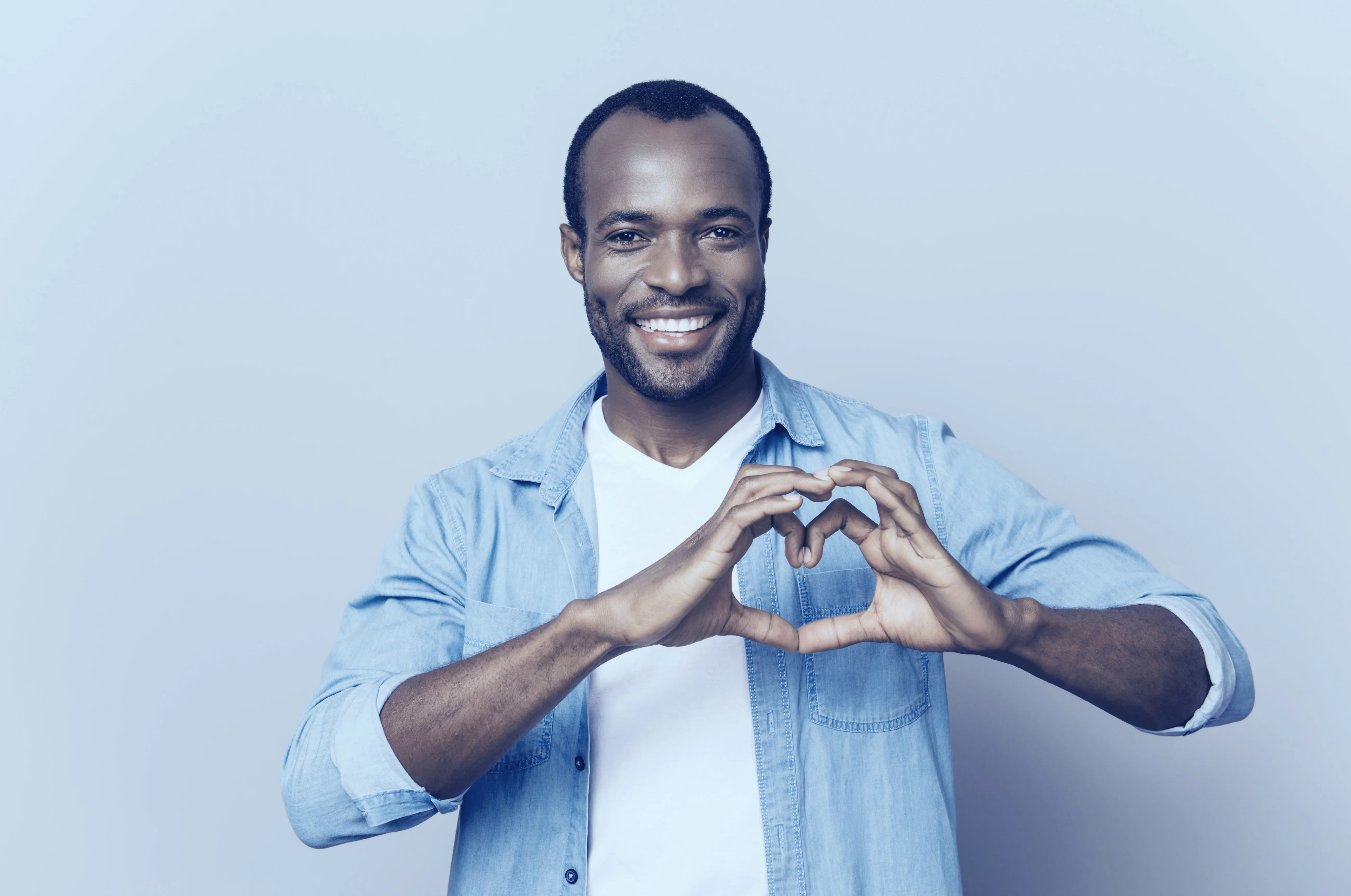 A smiling client in a denim shirt making a heart with his hands