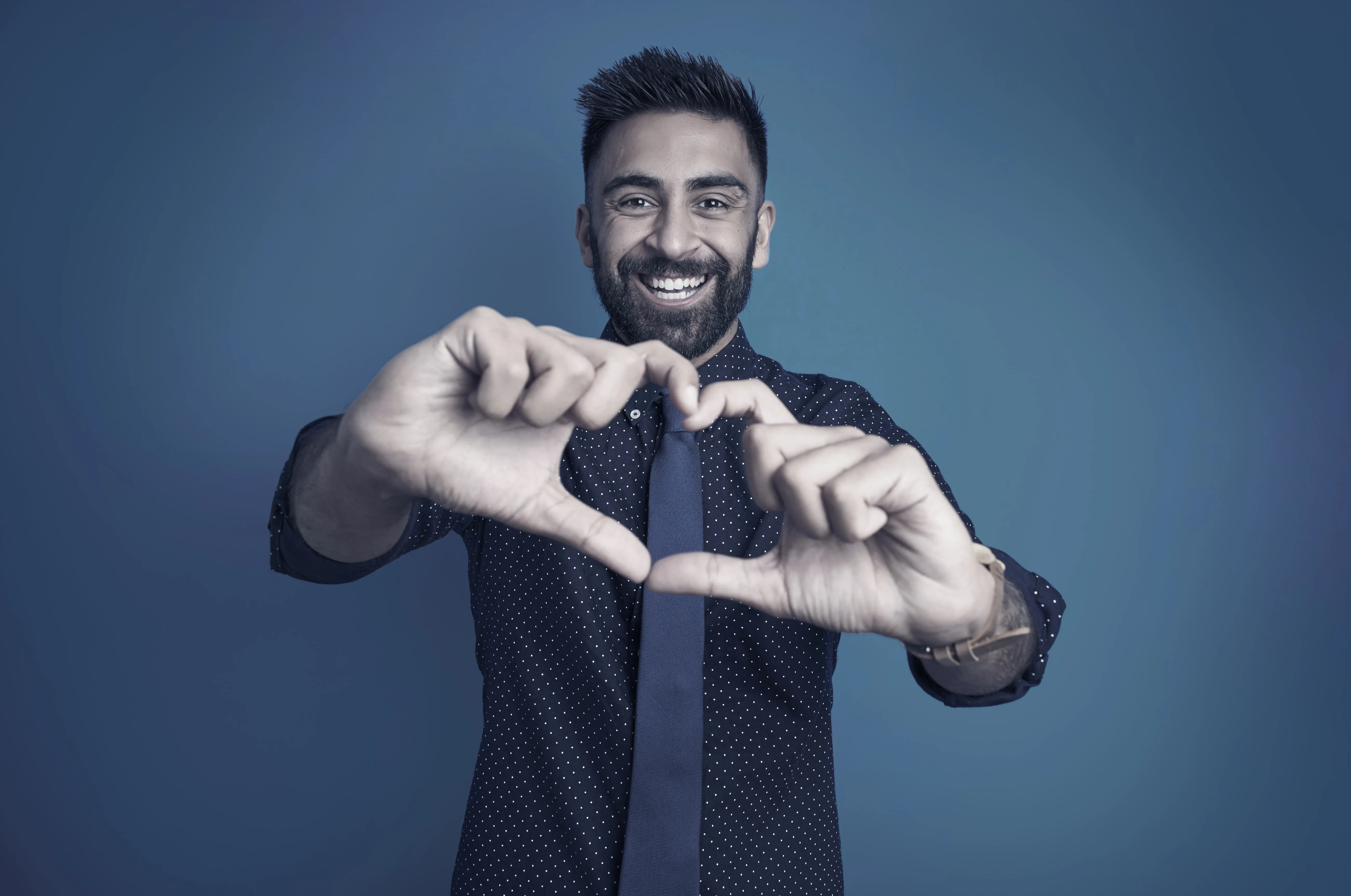 A smiling client in a shirt and tie making a heart with his hands