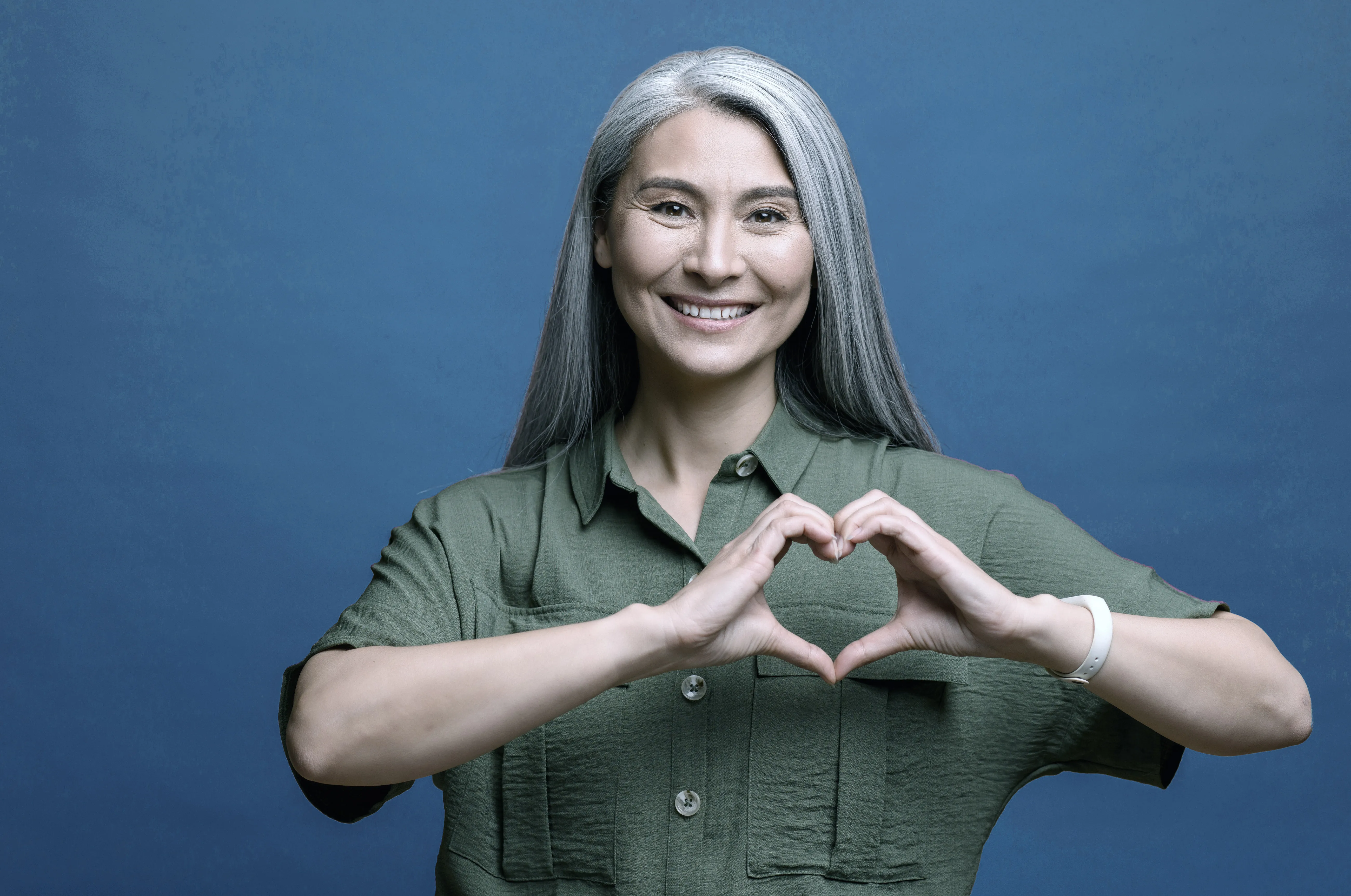 A smiling client with grey hair making a heart with her hands against a navy backdrop